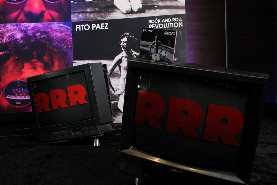 Escenografía del lanzamiento con la tapa del disco, el CD y la sigla RRR en televisores
