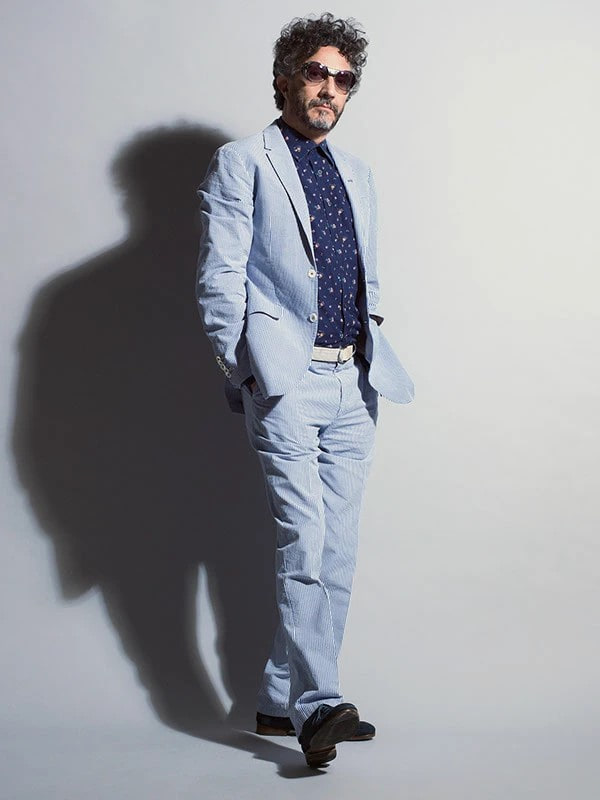 Fito Páez de traje celeste caminando frente a una pared gris