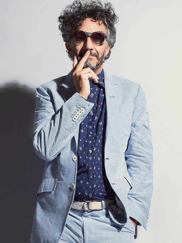 Fito Páez de traje celeste con la mano en el rostro